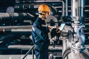 factory worker checking pressure valves with their equipment monitoring software