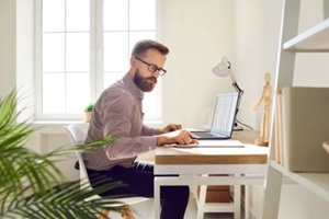focused male accountant working with paper documents and with tax planning software for electronic invoices on laptop