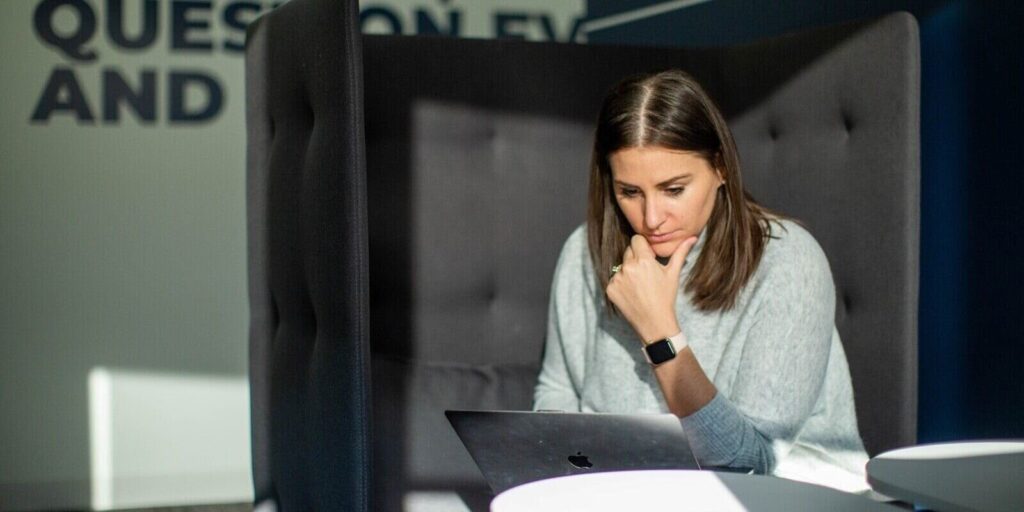 woman sitting in a modern office booth, focused on her laptop, with sunlight casting shadow
